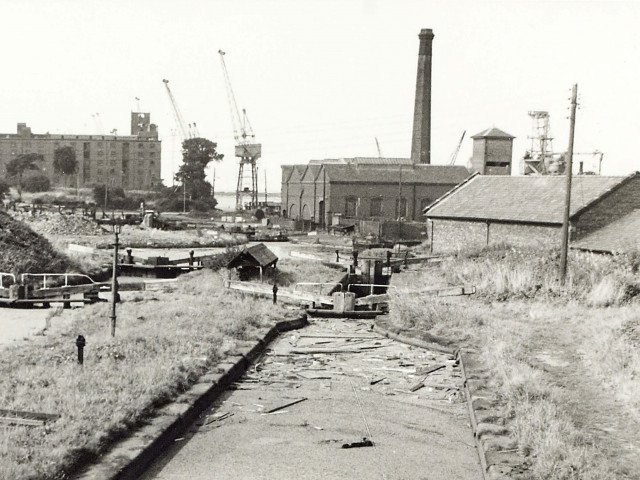 A view taken in 1971 showing the derelict Ellesmere Port Locks, on the Shropshire Union Canal, looking down towards the bottom basin with warehouses and cranes in the background. 