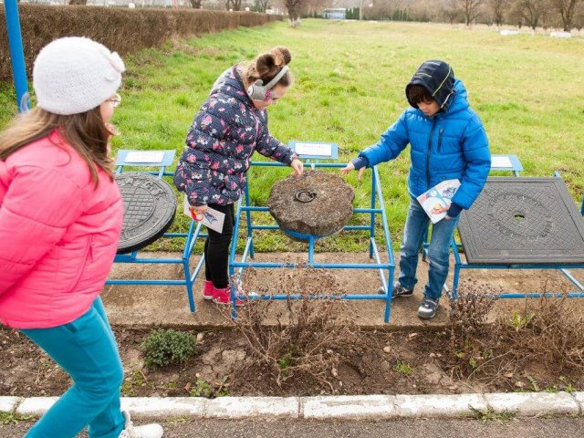 School pupils studying a stone manhole lid on “Manhole lids alley”, the other outdoor sections of the Museum, SOMES Water Company copyright, 2015