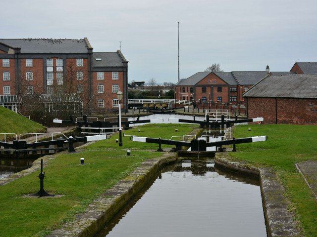 The same view taken in 2022 as the black and white photograph showing Ellesmere Port Locks on the Shropshire Union Canal, locking down towards the bottom basin.  The warehouses and cranes have been replaced with a hotel and residential accommodation.